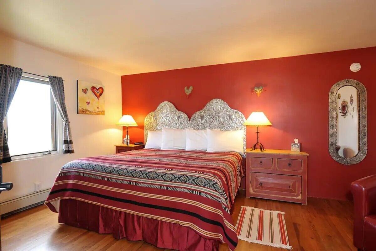 A bedroom with a large bed, two bedside lamps, a dresser, and a mirror on the wall.