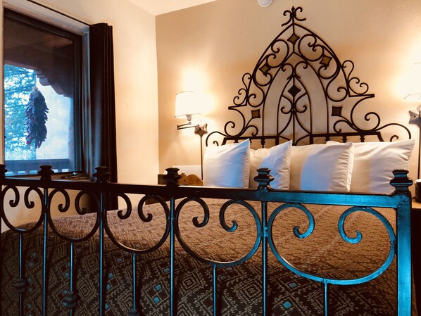 A bedroom with a metal headboard, a window with a view of trees, and a patterned carpet. - Casa Cuma Bed & Breakfast (Santa Fe)