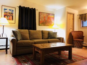 A living room with a sofa, a coffee table, a chair, a lamp, a painting, and a door. - Casa Cuma Bed & Breakfast (Santa Fe)