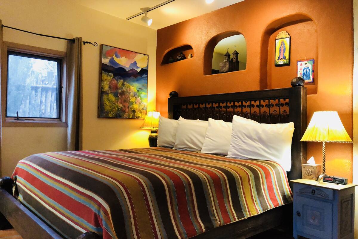A hotel room with a large bed, a nightstand with a lamp, a painting on the wall, and a window with a view.