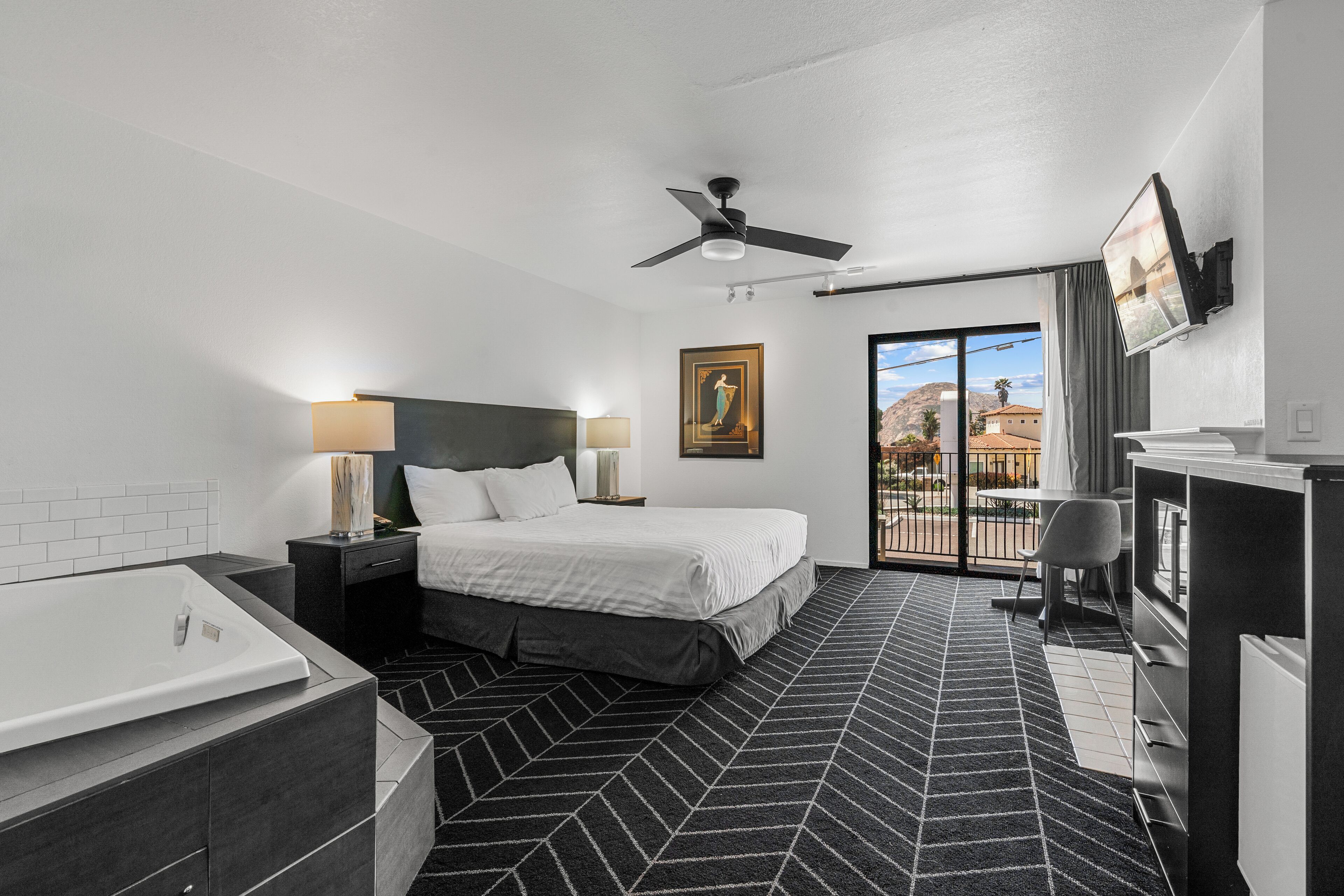 Una habitación de hotel moderna con una cama grande, un baño independiente con bañera, un escritorio con silla y un televisor montado en la pared.