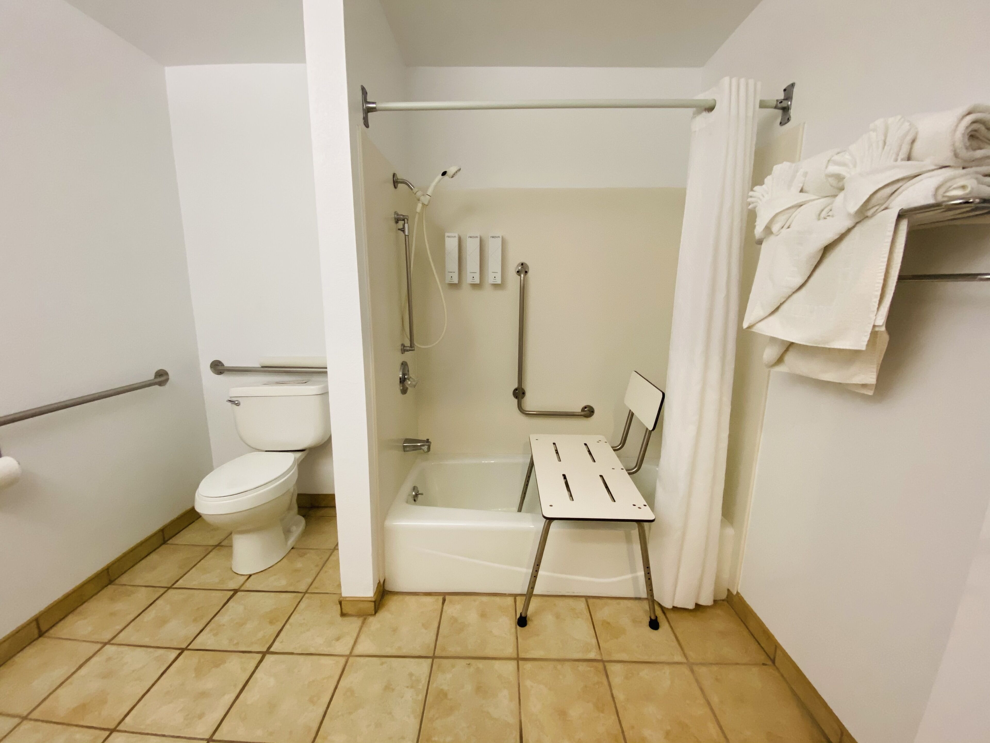 Ein Badezimmer mit Toilette, einer Dusche mit Haltegriff und einer kleinen Sitzbank.