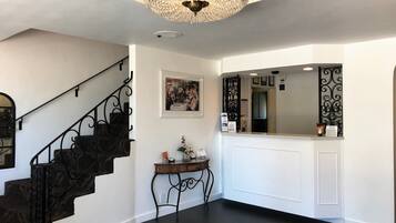 A staircase with a black metal railing, a chandelier, a framed picture on the wall, and a reception desk with a mirror.