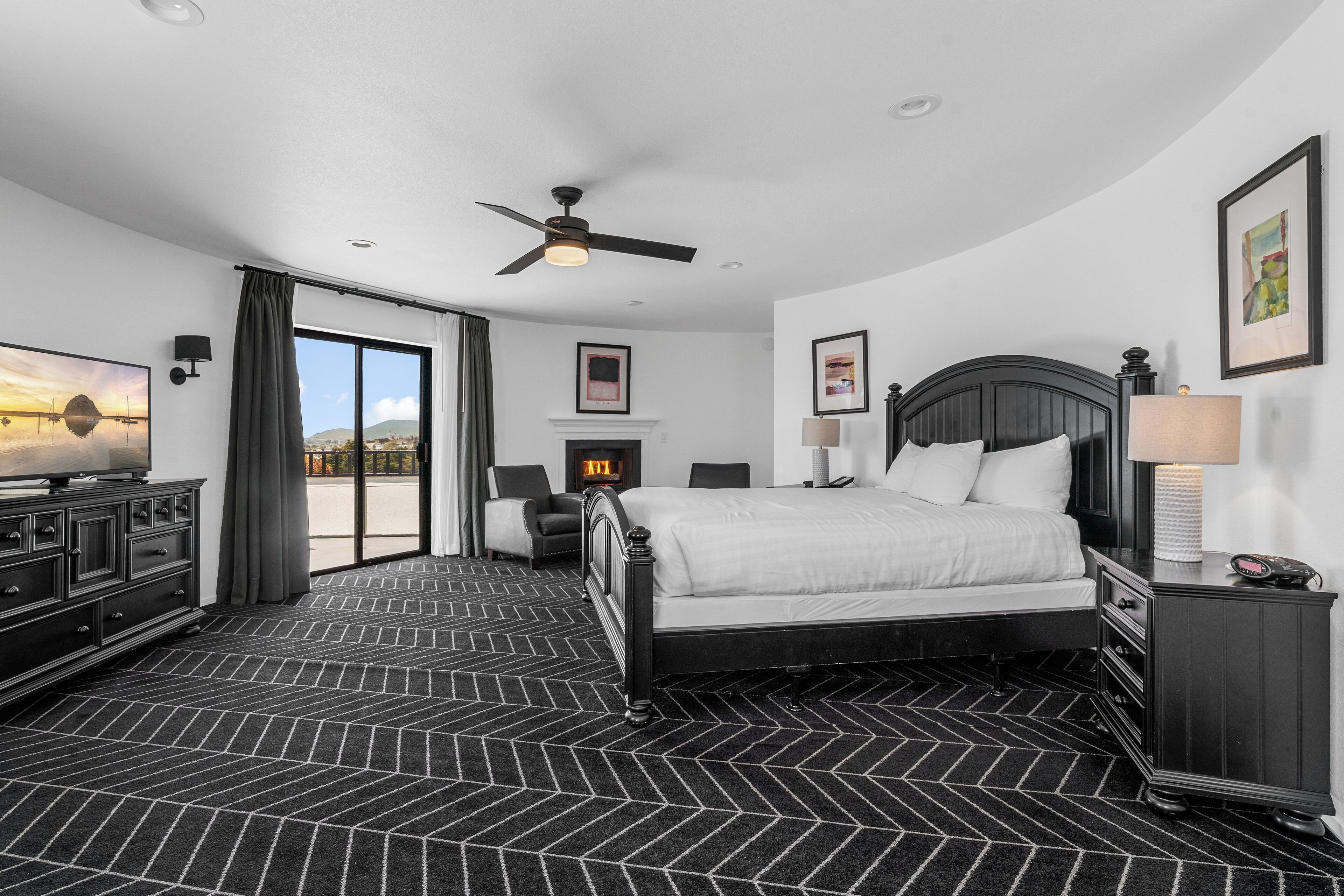 Quarto de hotel com cama, ventoinha no teto, lareira, televisão e vista para o exterior.