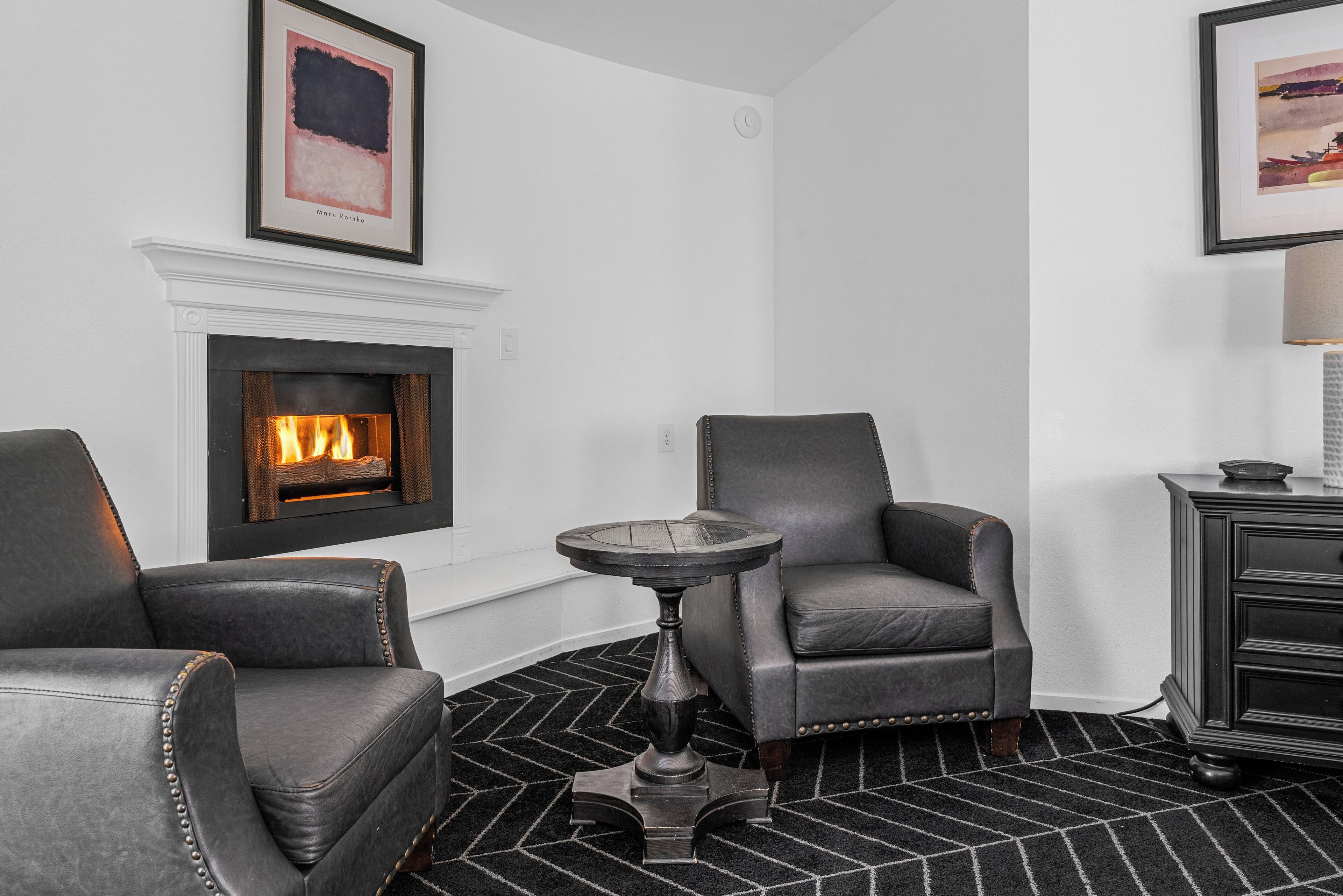 Una sala de estar con chimenea, dos sillones de cuero, una mesa de centro redonda y un tapete con estampado en blanco y negro.