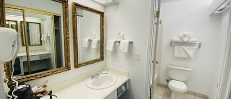 Ein Badezimmer mit einem weißen Waschbecken, zwei Spiegeln mit aufwendigen Rahmen, einem Fön und einem Handtuchhalter.