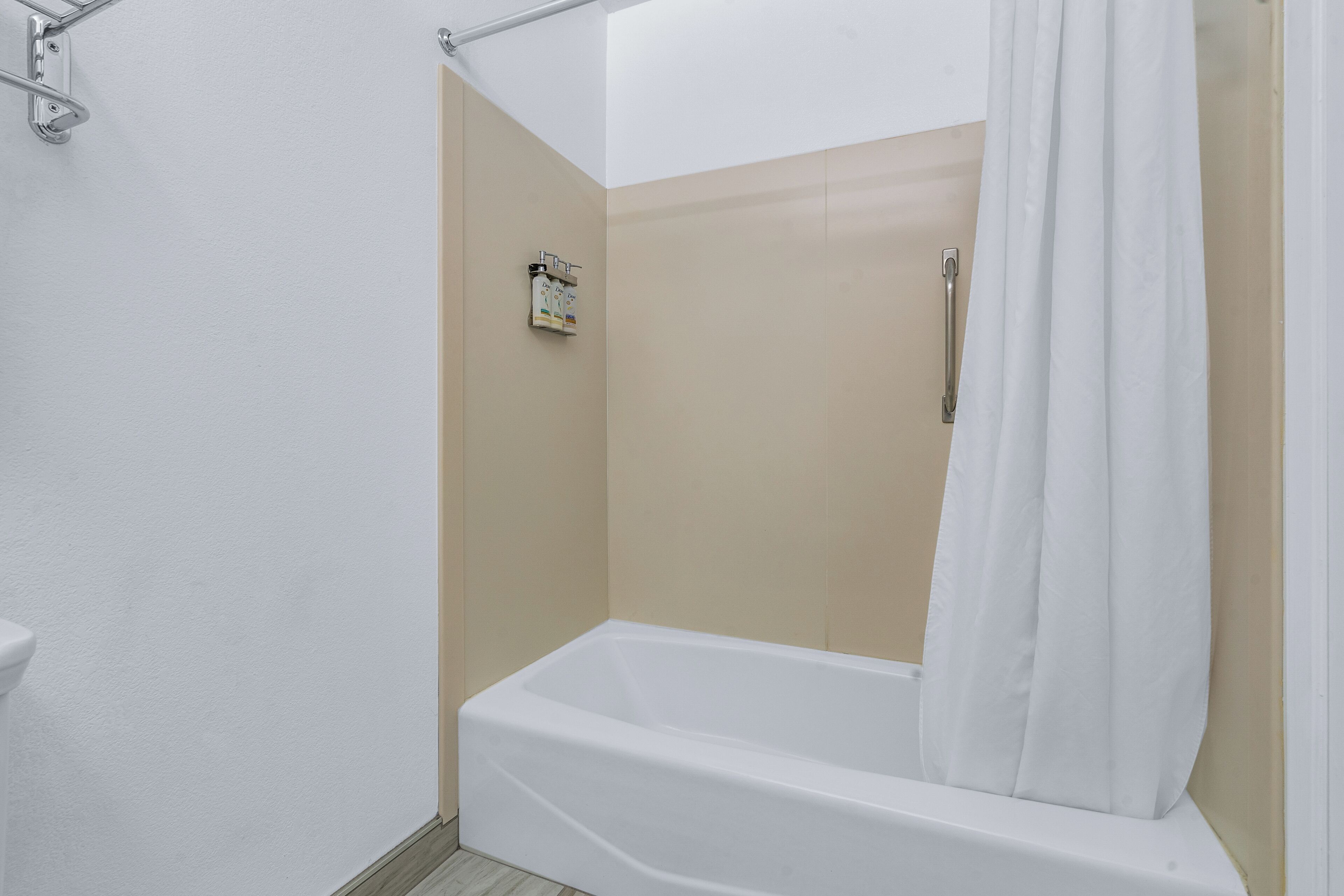Doccia angolare con tenda bianca, pareti color beige e vasca da bagno bianca.