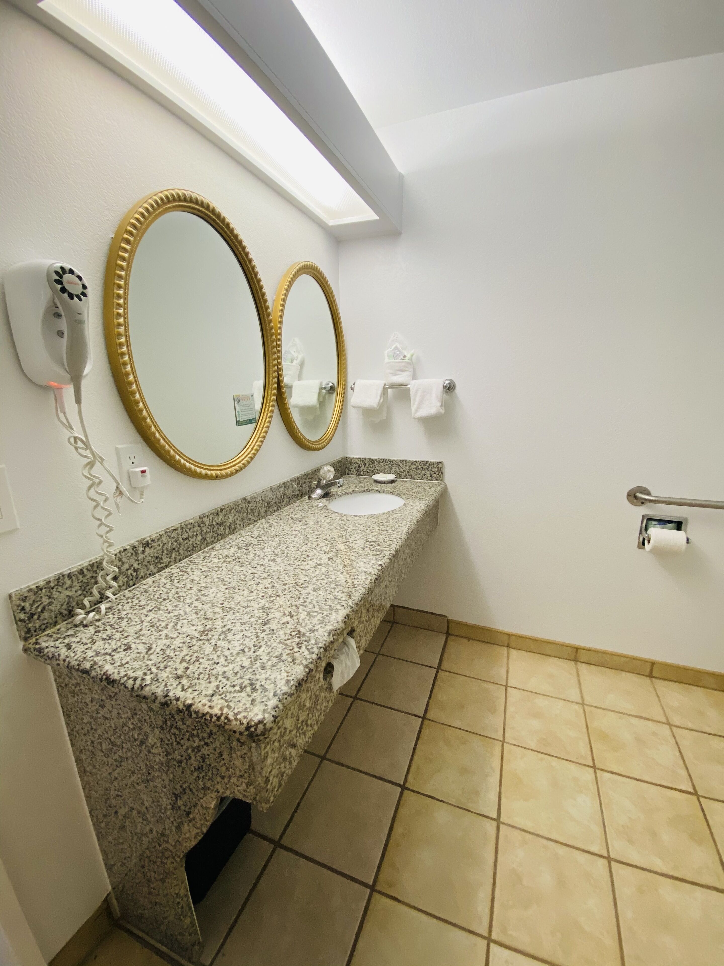 A bathroom with a granite countertop, two gold-framed mirrors, a white sink, a towel rack, and a hand dryer.