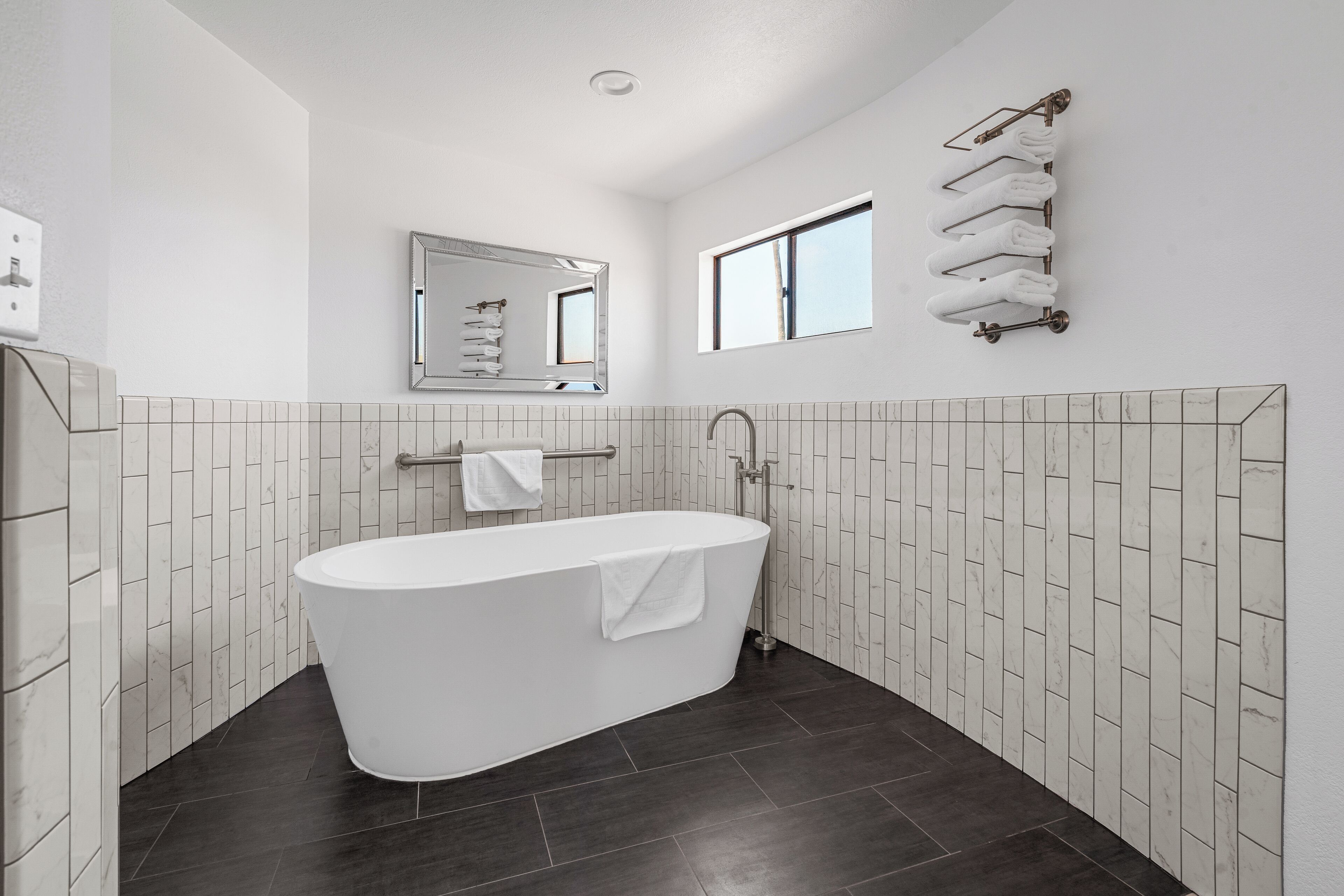 Un baño moderno con una bañera independiente, un espejo grande y un perchero para toallas.