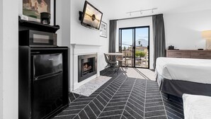 Una habitación de hotel moderna con chimenea, un televisor de pantalla plana montado en la pared, una cama, un área de comedor con mesa y sillas, y un balcón con vistas.