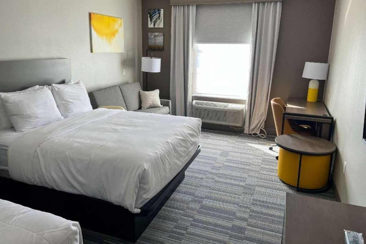 A hotel room with a large bed, a desk, a chair, a lamp, and a window with curtains.