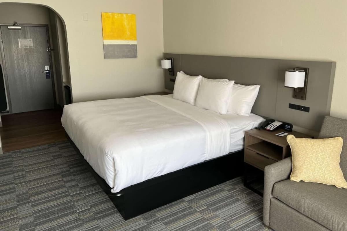 A hotel room with a large bed, bedside lamps, a desk with a phone, and a sofa with a pillow.