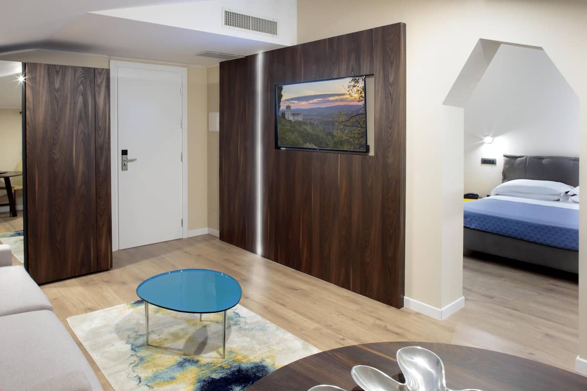 A modern hotel room with a bed, a desk, and a TV mounted on the wall.