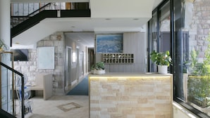 Un vestíbulo de hotel con mostrador de recepción de piedra, una escalera, un ventanal con vistas a la ciudad y un televisor fijado a la pared.