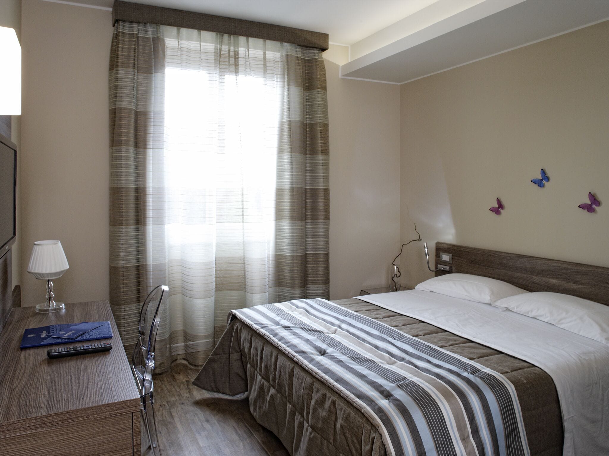 Ein Hotelzimmer mit Bett, Nachttisch, Lampe und Vorhängen.