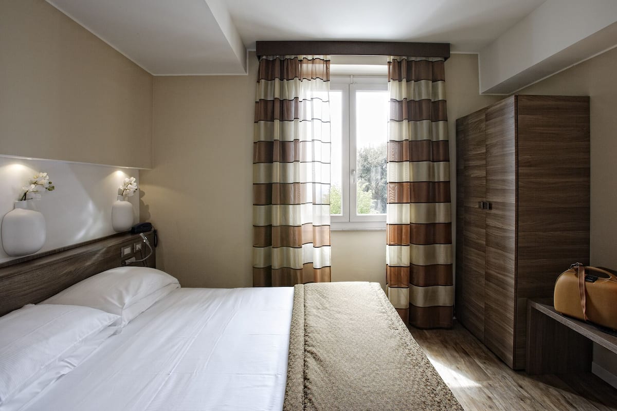 A bedroom with a bed, a nightstand, a wardrobe, and a window with curtains.