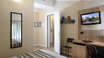 A hotel room with a bed, a desk with a chair, a TV, and a wall-mounted clock.