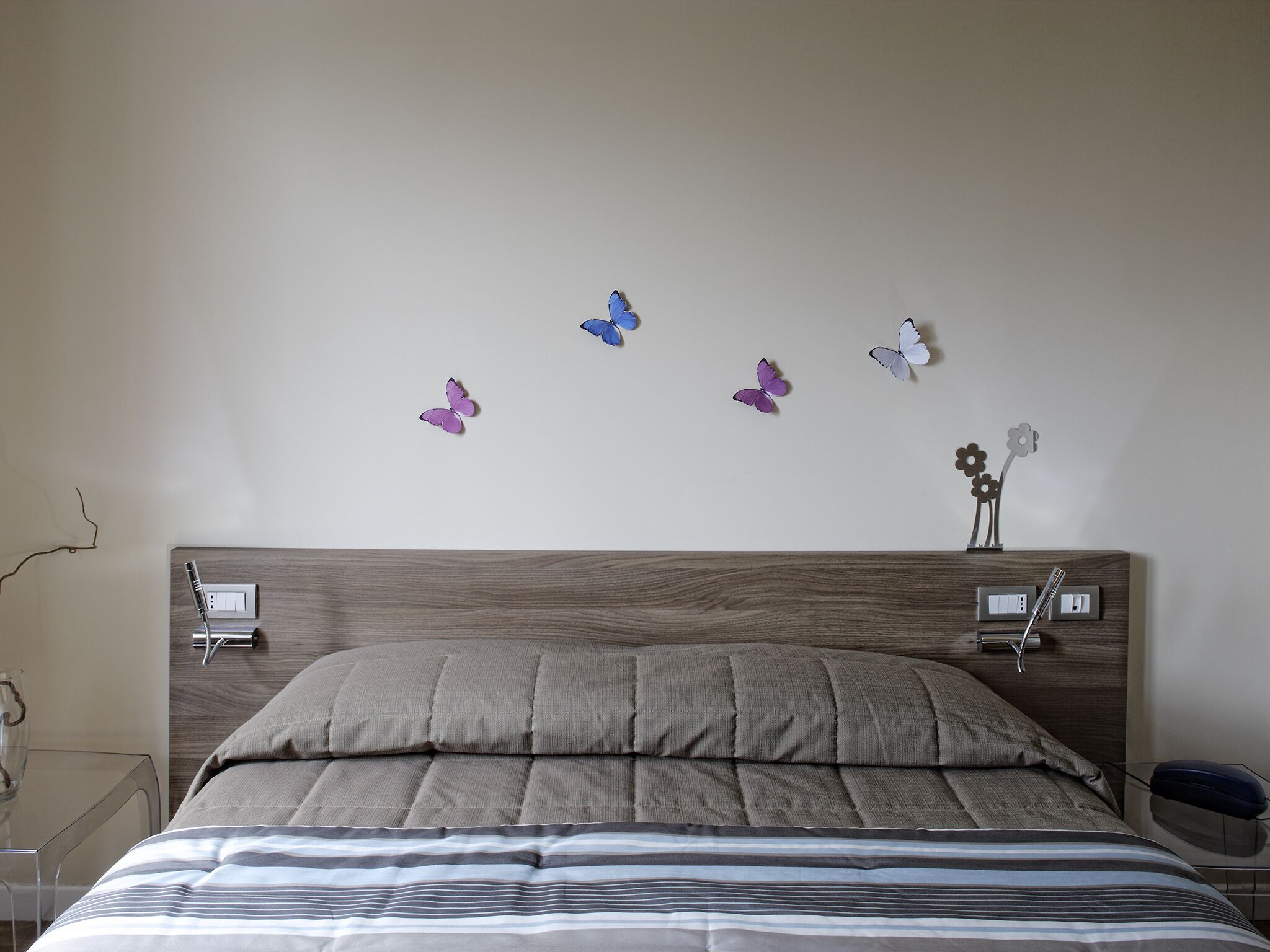 A bedroom with a wooden headboard, a bed with striped bedding, and wall-mounted light switches.