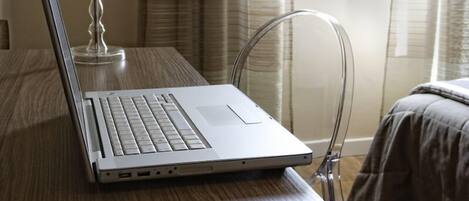 A laptop on a wooden table with a lamp beside it, near a window with curtains.
