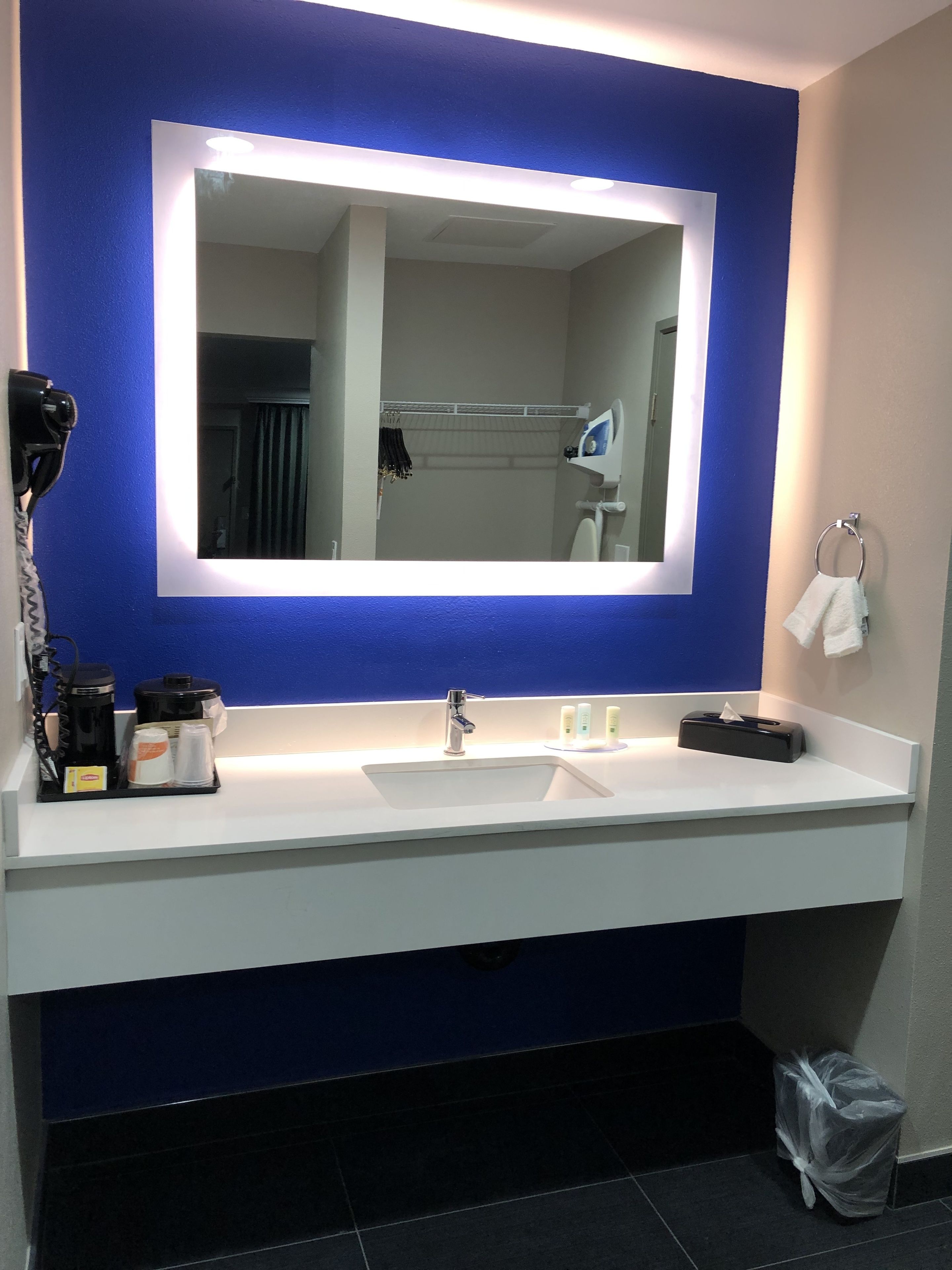 A bathroom with a large mirror, two sinks, a hairdryer, and toiletries on the counter.
