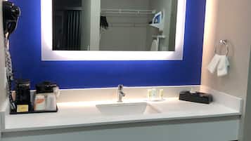 A bathroom with a large mirror, two sinks, a hairdryer, and toiletries on the counter.
