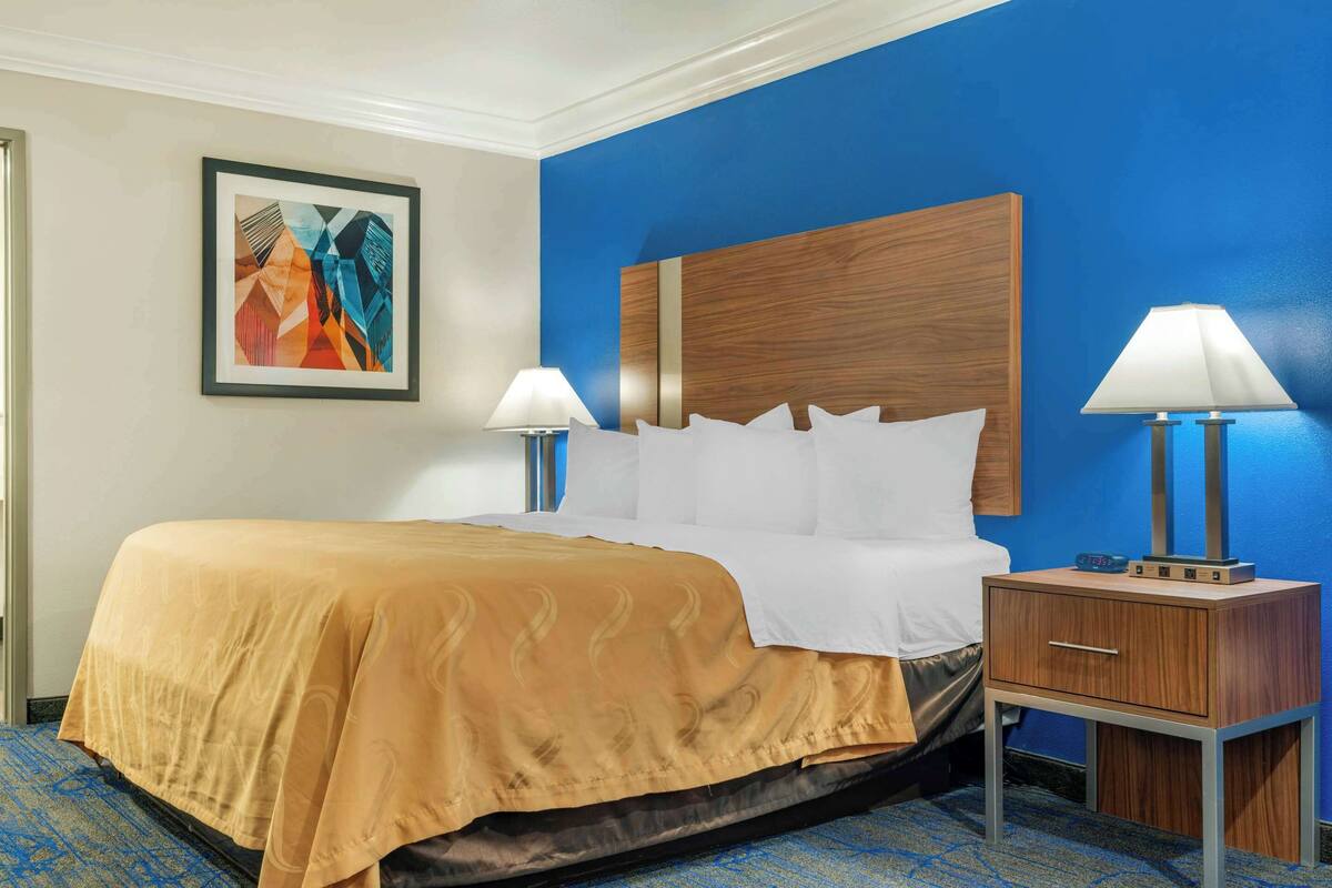 A hotel room with a large bed, two bedside lamps, a wooden nightstand, and a framed artwork on the wall.