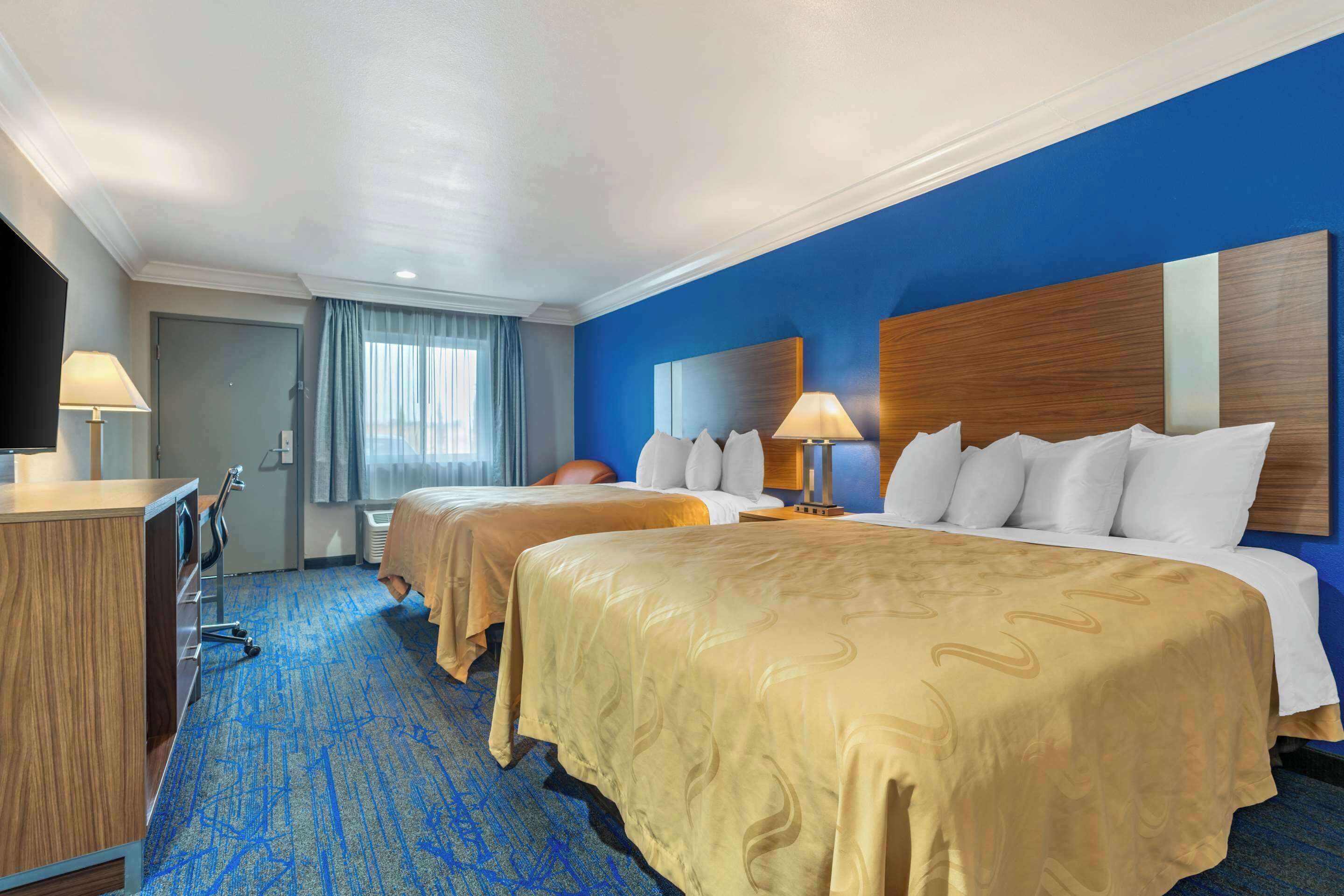 A hotel room with two beds, a desk, and a television.
