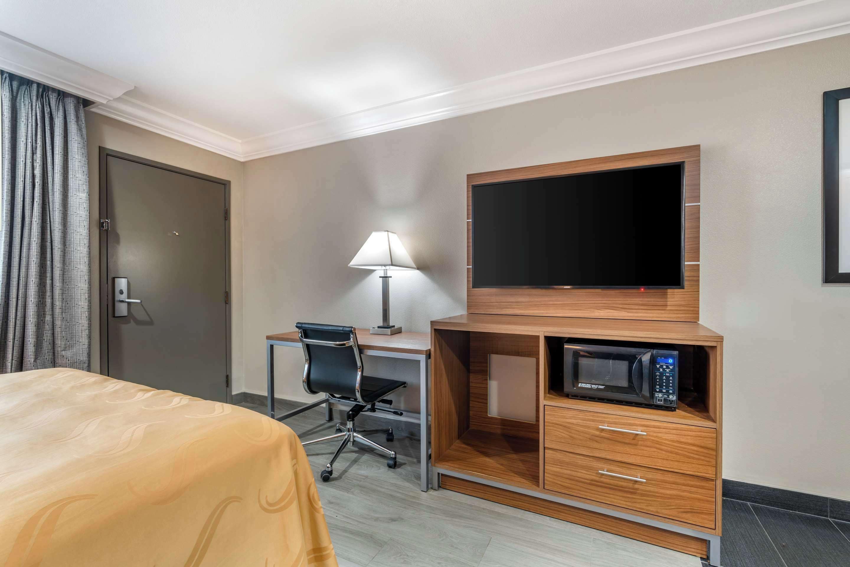 Una habitación de hotel con una cama, un escritorio con una silla, un televisor y un microondas.