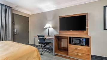 Una habitación de hotel con una cama, un escritorio con una silla, un televisor y un microondas.