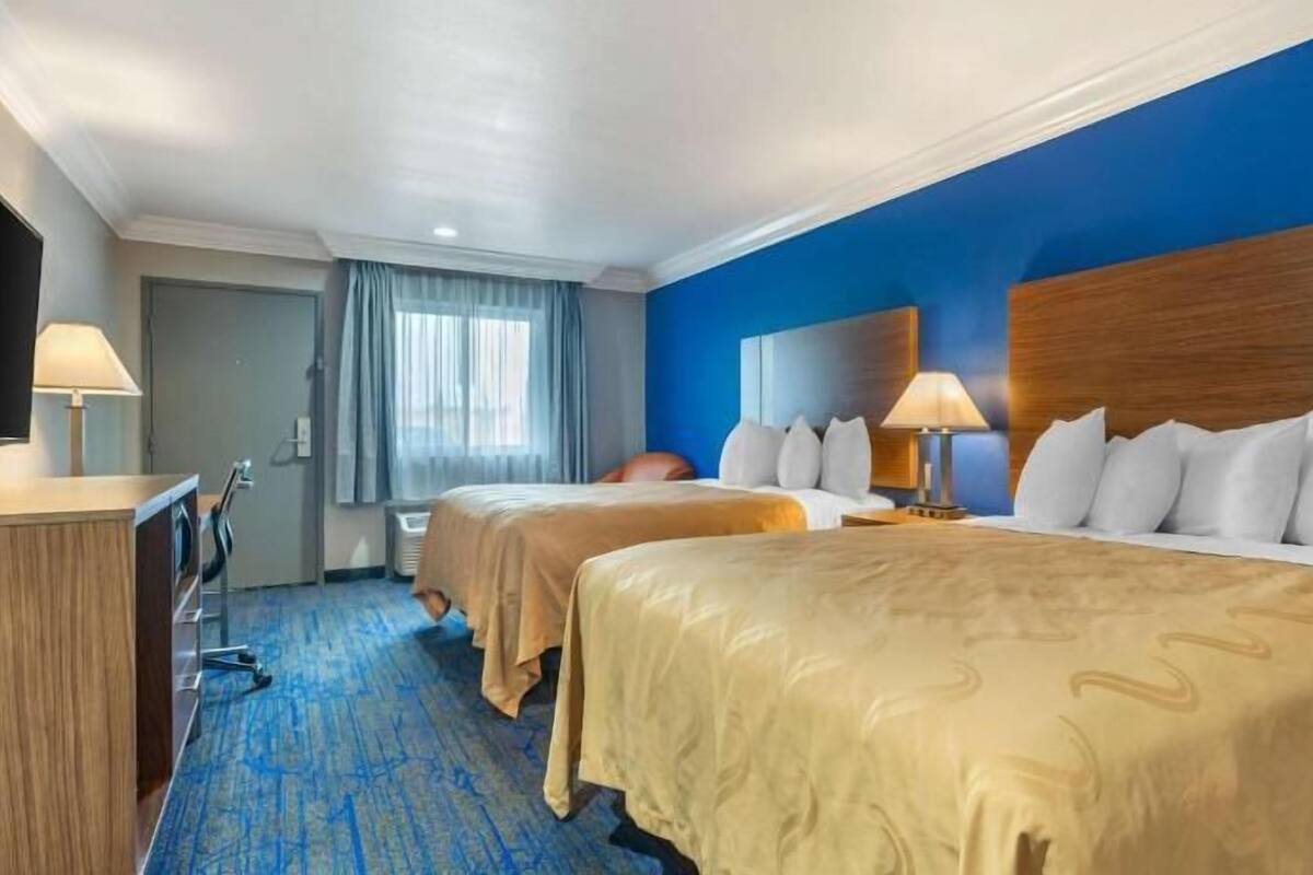A hotel room with two beds, a desk, a chair, and a TV.