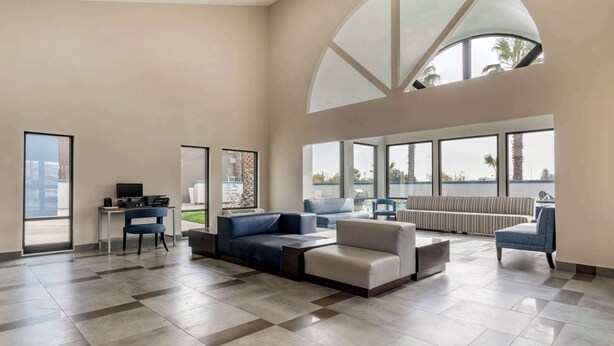 A spacious living area with a large window, a sofa set, a desk with a computer, and a view of the outdoors.
