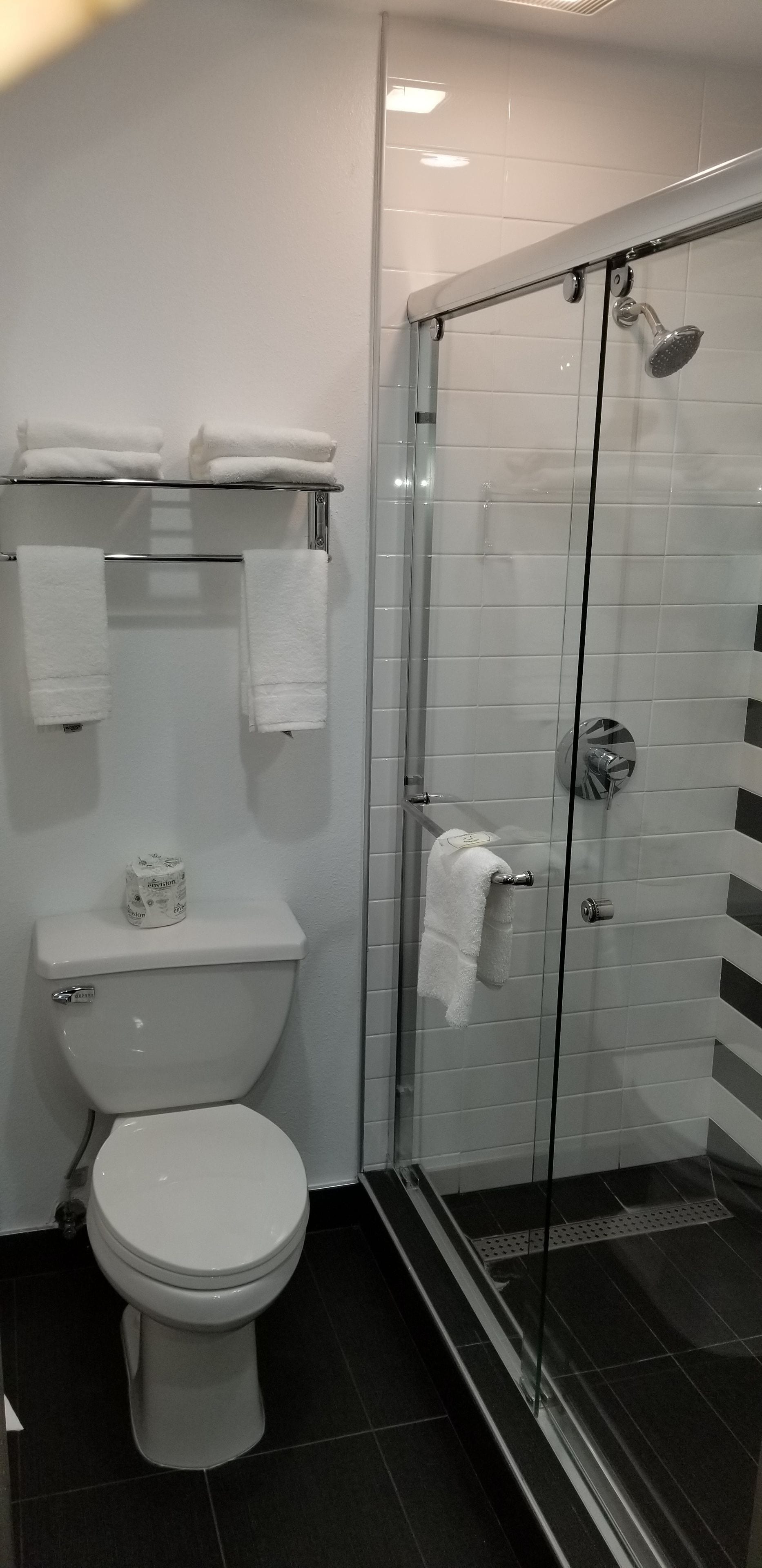 A modern bathroom with a toilet, a glass shower enclosure, and a towel rack with towels.