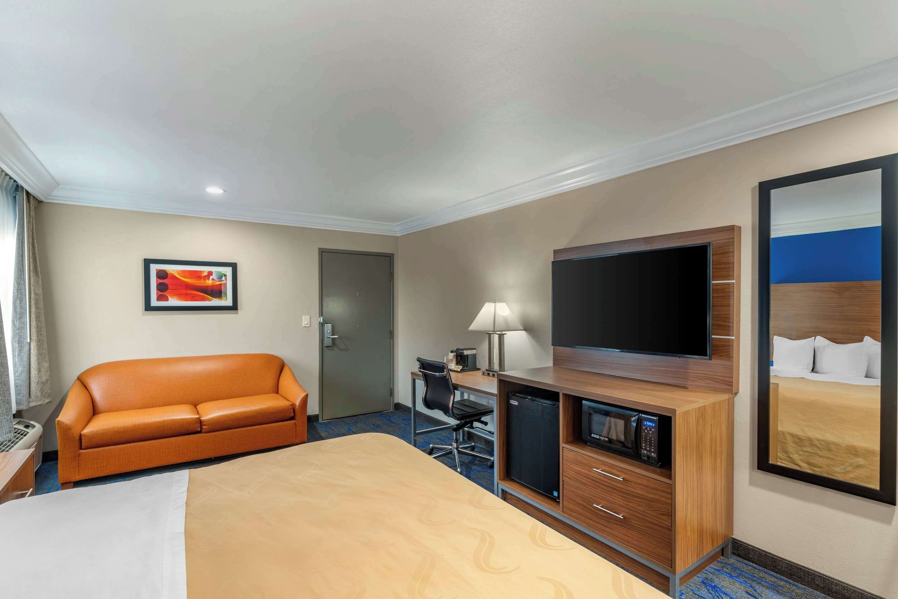 Habitación de hotel con una cama, un escritorio con computadora, televisión, sofá y espejo.