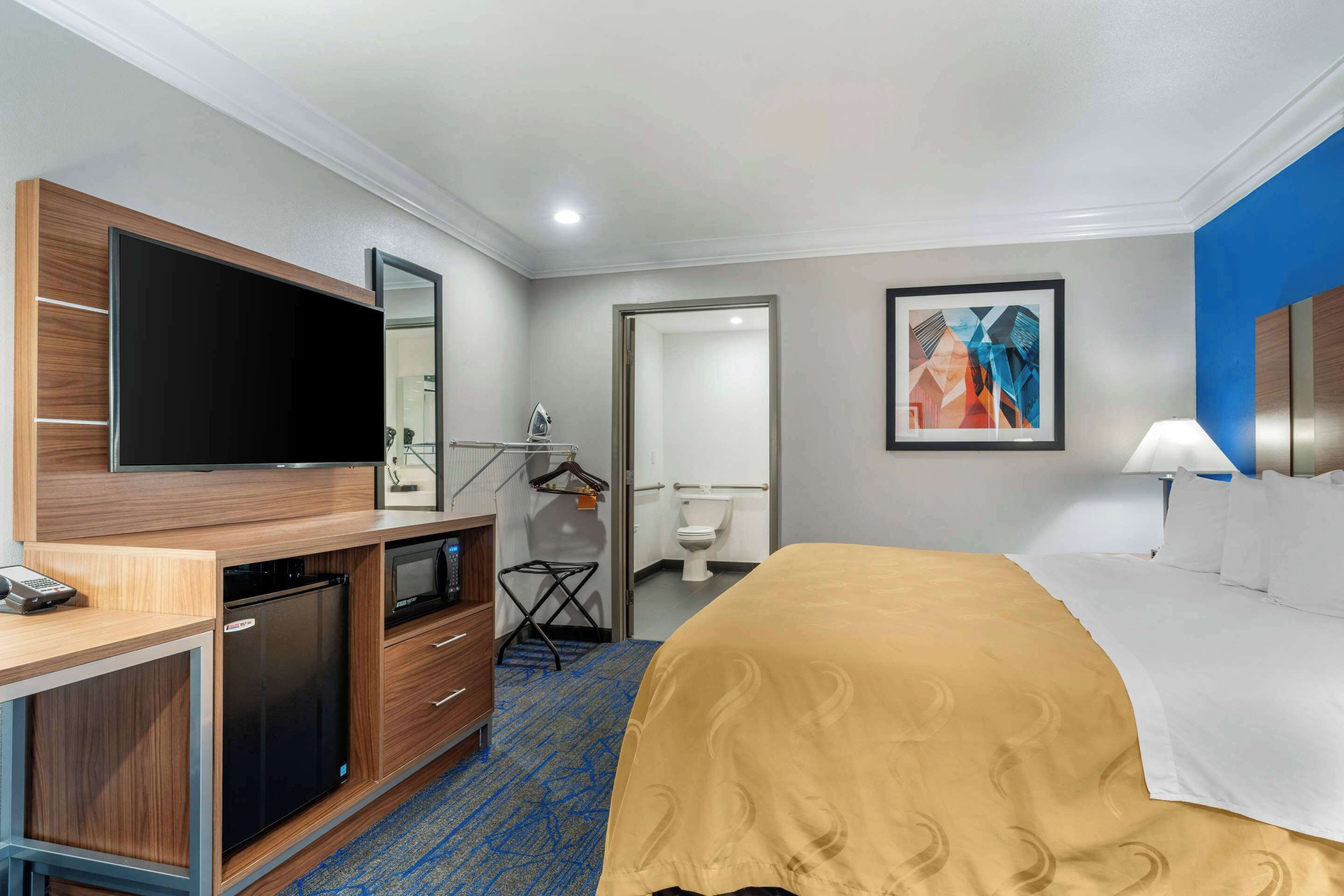 A hotel room with a bed, a TV, a desk with a microwave, and a bathroom visible through an open door.