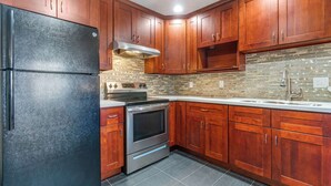 A kitchen with wooden cabinets, a black refrigerator, a stainless steel oven, and a tiled backsplash.