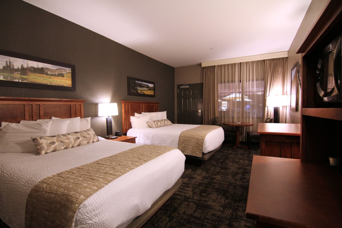A hotel room with two beds, a desk, a chair, a lamp, and a painting on the wall.