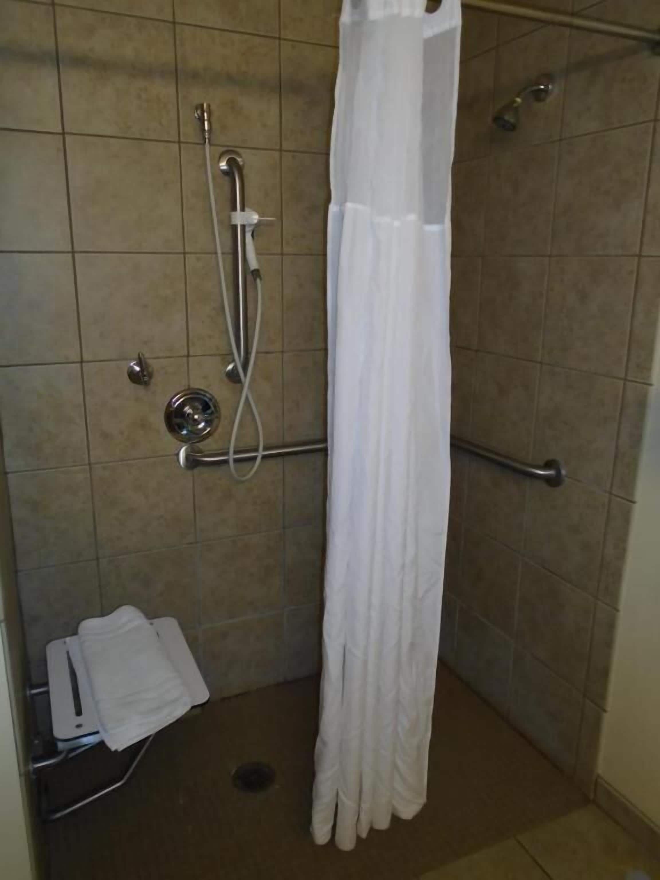 Área de duche com cortina branca, barras de apoio e chuveiro manual.