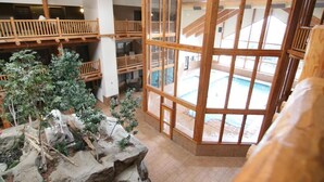 A multi-level wooden interior with a central rock garden and a large window overlooking an outdoor swimming pool.