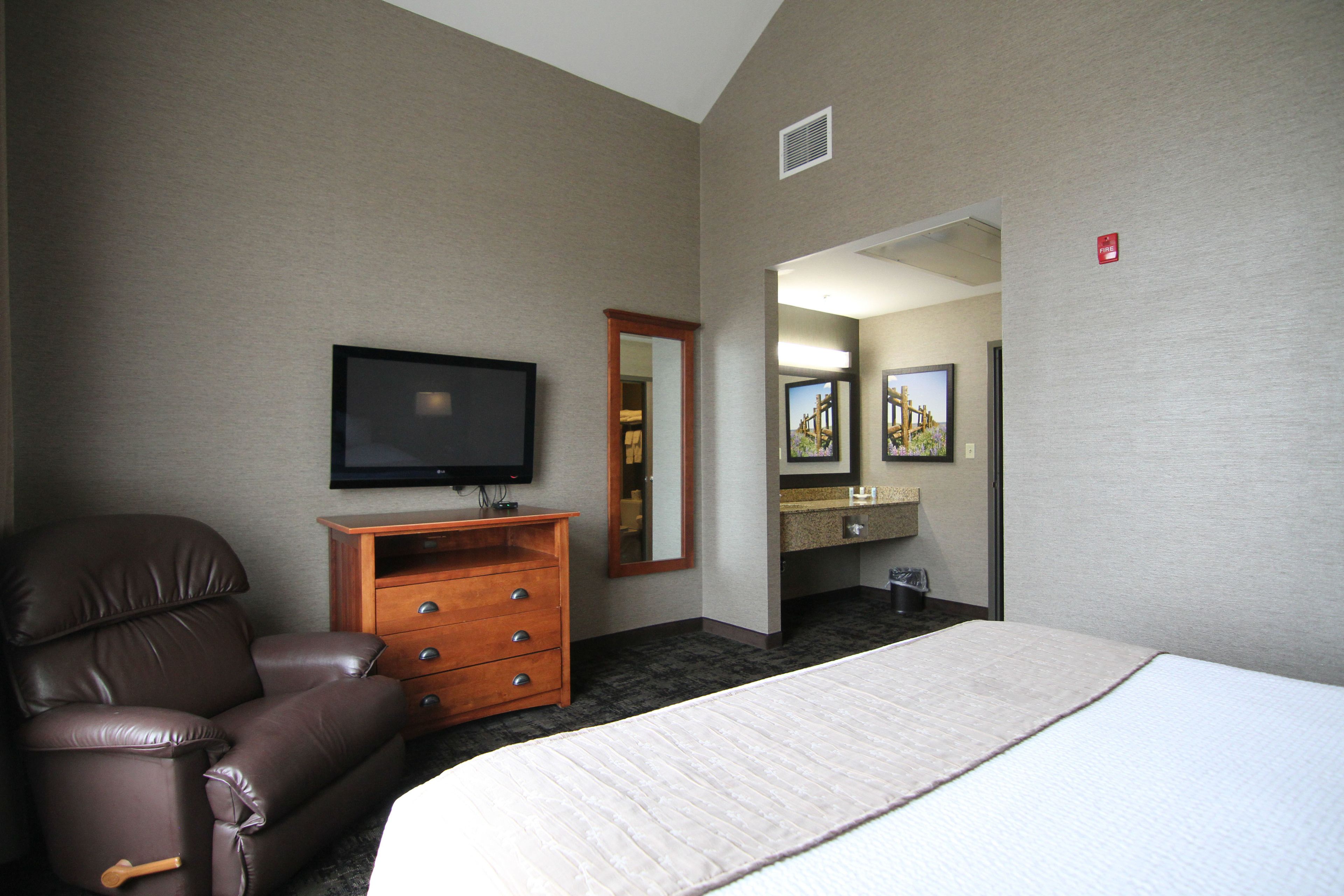 A hotel room with a bed, a leather chair, a TV, a dresser, and a bathroom visible through an open door.