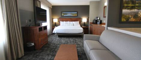 A hotel room with a bed, a sofa, a TV, a desk, and a painting on the wall.