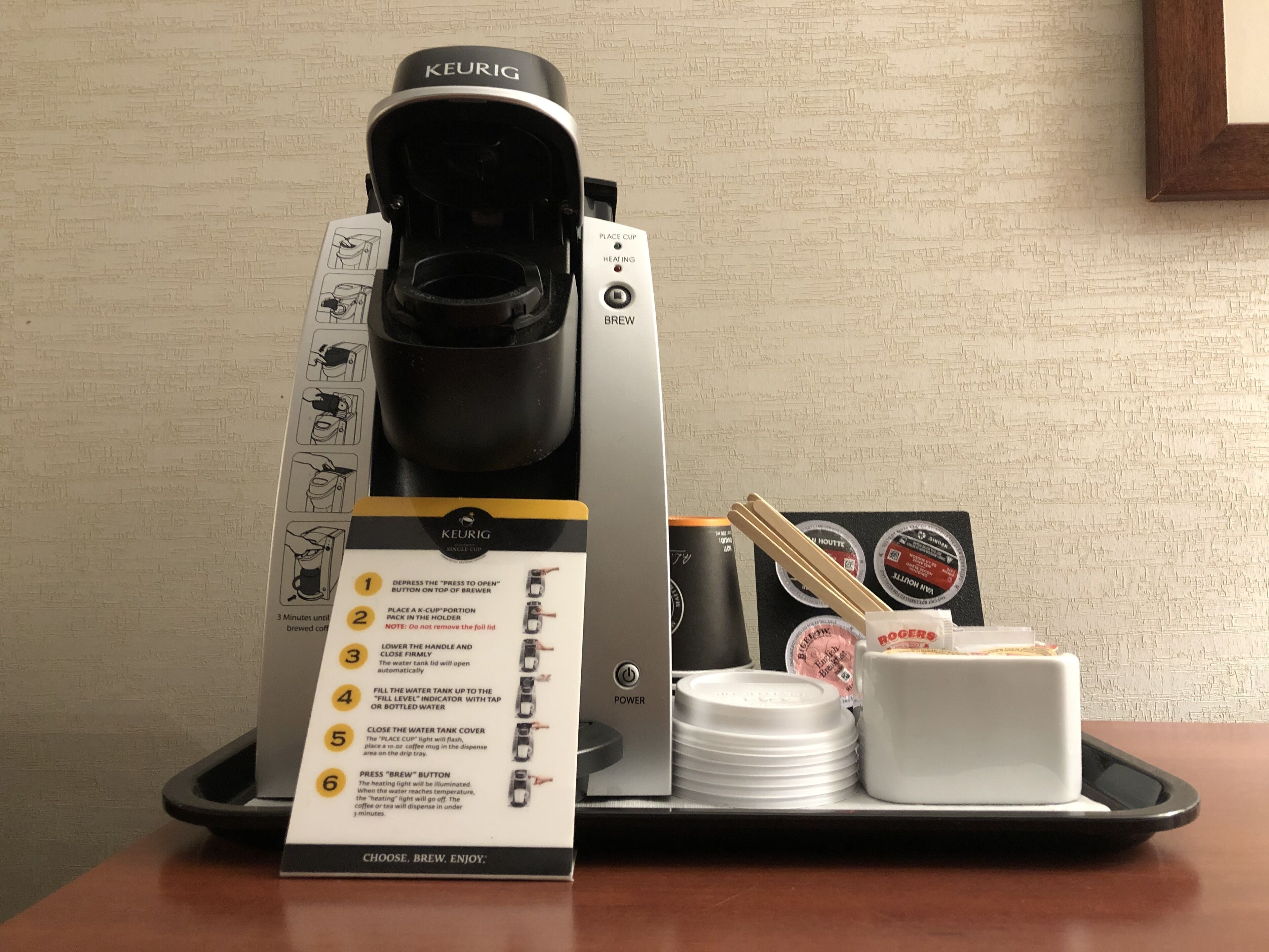 Una cafetera Keurig con un manual, un porta K-Cup, una pila de platos blancos y una taza blanca pequeña sobre una bandeja.