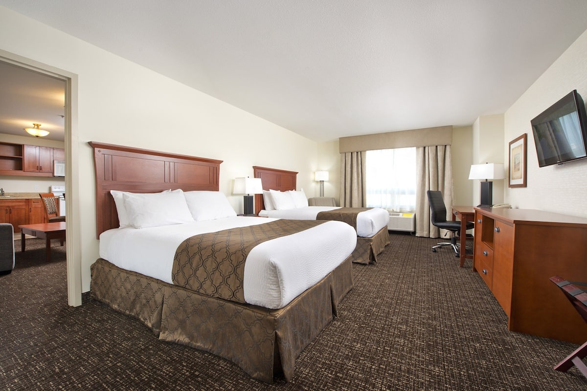 A hotel room with two beds, a desk, a chair, a television, and a view of the city.