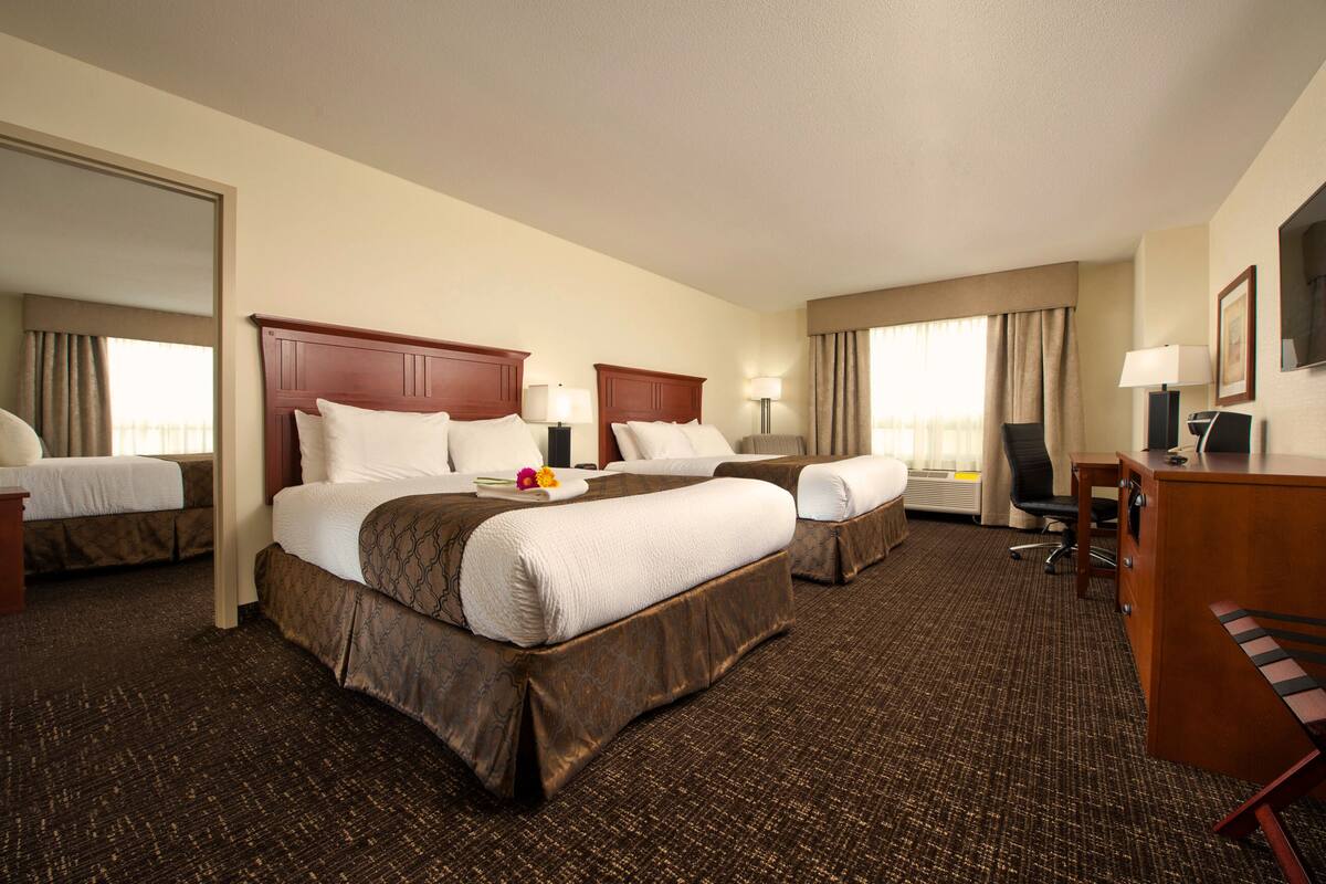 A hotel room with two beds, a desk, a chair, and a television.