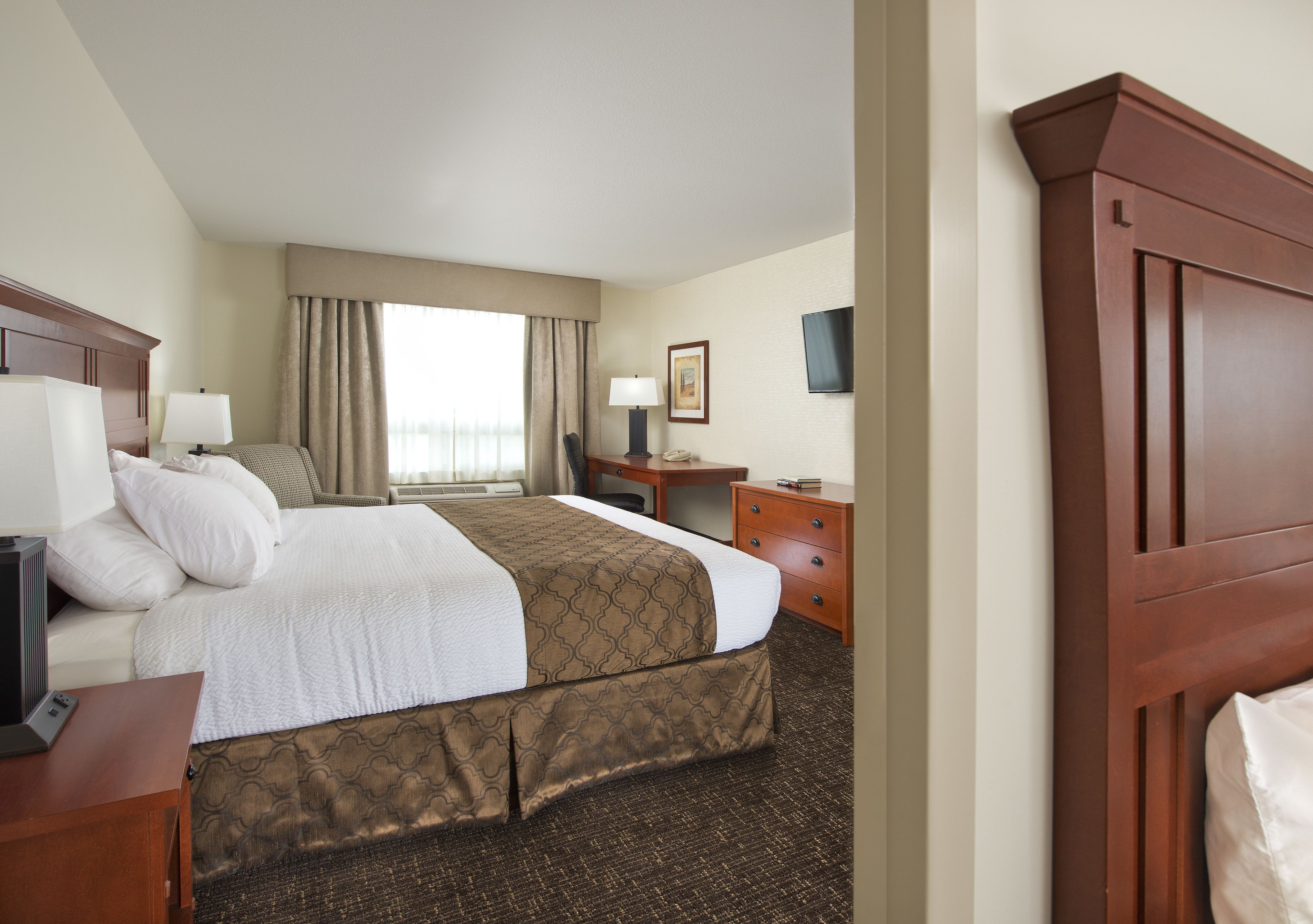 A hotel room with a large bed, a desk, a chair, a television, and a window with curtains.