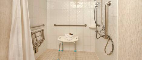 A shower area with a grab bar, a white towel on a small stool, and a handheld showerhead.