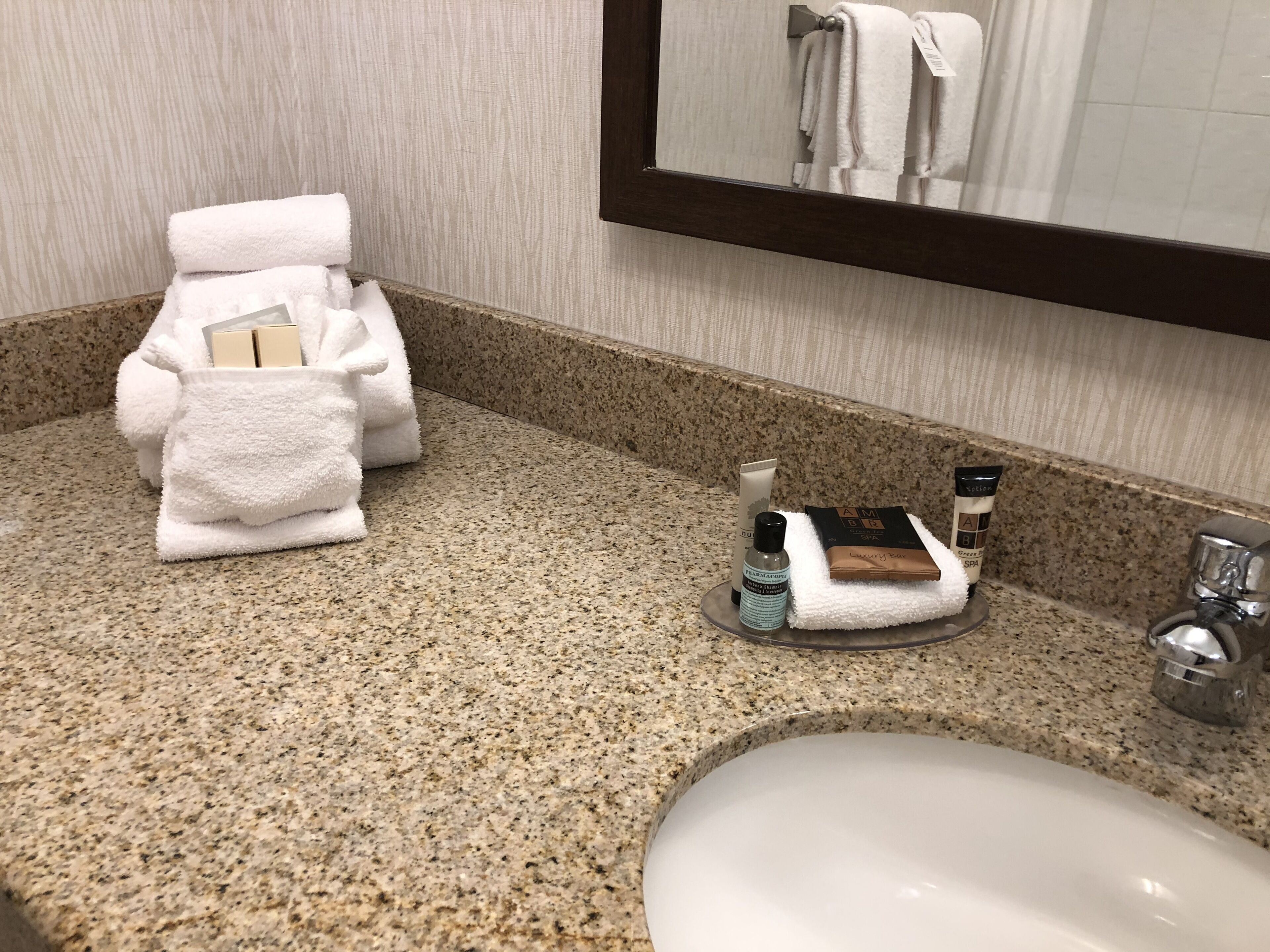 A bathroom with a granite countertop, a white sink, and toiletries including a bottle of lotion and a tube of cream.