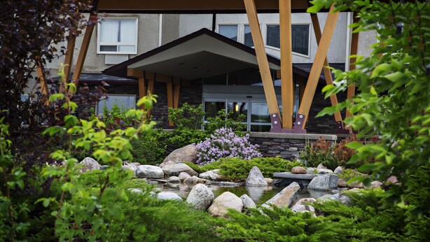 A modern house with a stone facade, a landscaped garden with a pond, and wooden beams supporting the roof.