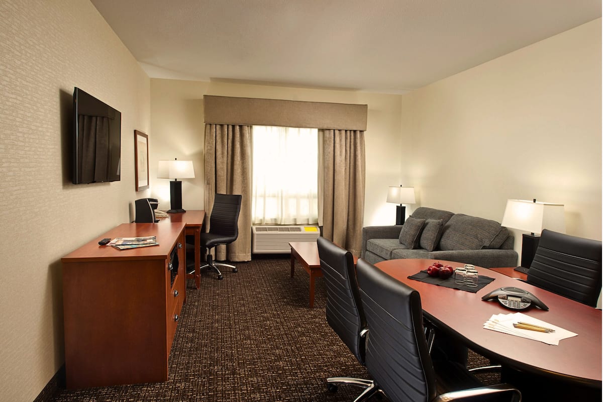 A hotel room with a desk, two chairs, a sofa, and a TV.