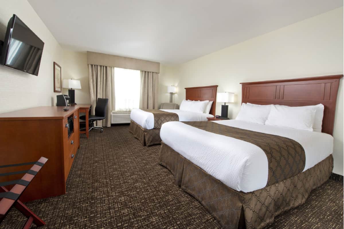 A hotel room with two beds, a desk, a TV, and a chair.