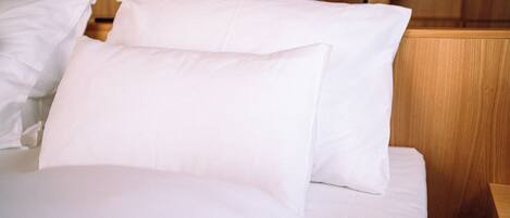 A neatly made bed with white linens and pillows in a room with wooden furniture and a lamp.